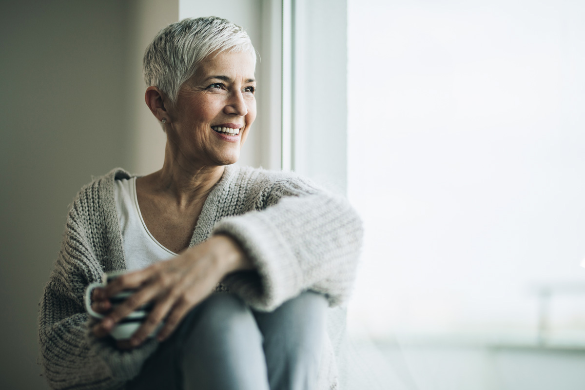 Mujer 50 años sonriendo mirando al infinito en su habitacion